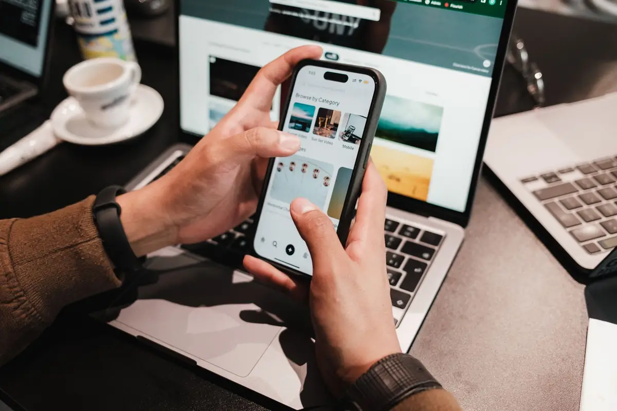 Hands searching on a smartphone beside a laptop